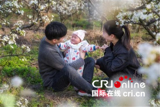 中國春分遇上國際幸福日 幸福如花般綻放_fororder_信陽市商城縣鄢崗梨園，村裏的小夫妻，帶著滿百天的幼子，享受春天的美好【攝影：余敦梅】